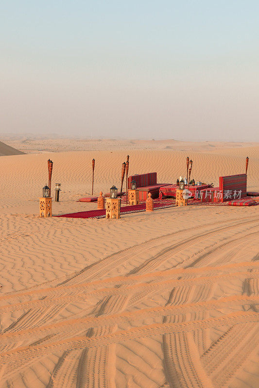 沙漠晚餐在沙丘上铺设地毯和靠垫，为日落浪漫晚餐做好准备