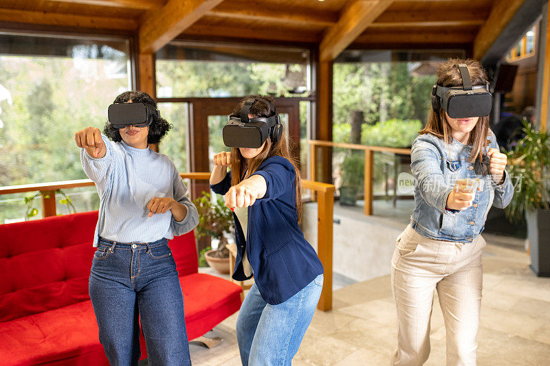 三位年轻女性在客厅享受虚拟现实，女性朋友使用新技术玩游戏，戴着增强现实头盔模拟武术动作