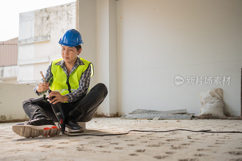 建筑工人在施工现场使用电动手提钻打孔设备，在浇筑地面前打孔，使地面坚固，工人和住宅建筑的概念。