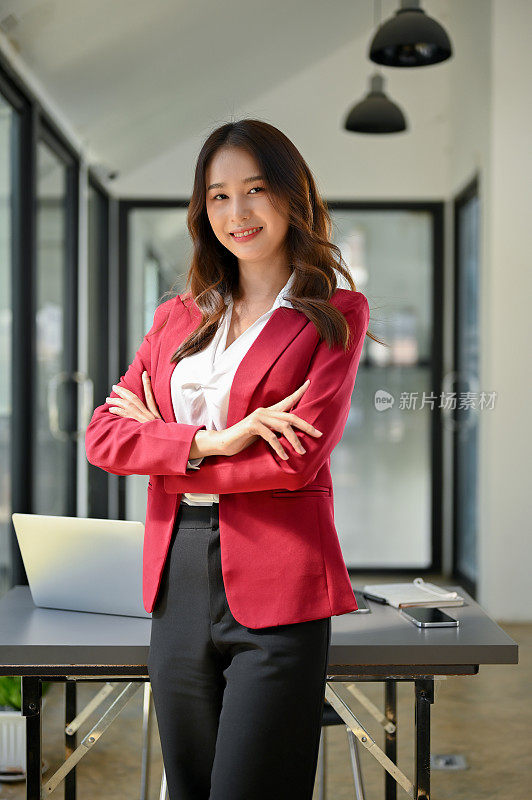华丽和成功的千禧一代亚洲女商人站在她的办公室，双臂交叉