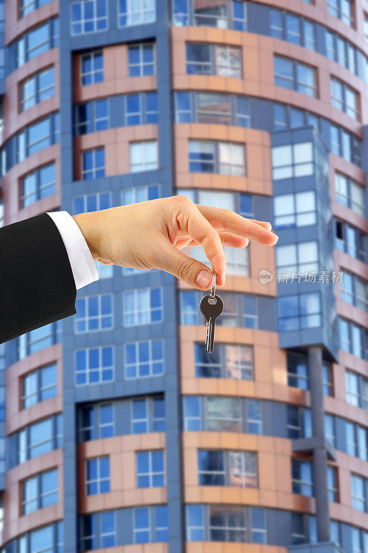 在一栋多层建筑的背景下，一只手拿着购买的公寓的钥匙