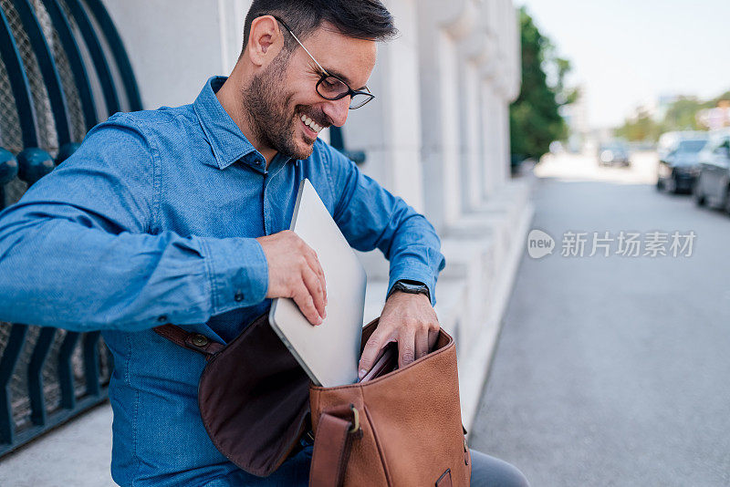 满意的英俊的成年商人，把他的笔记本电脑装在手提包里。