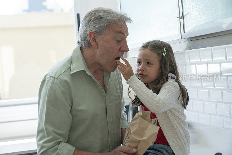 老人和孙女在家里的厨房里吃爆米花，玩得很开心