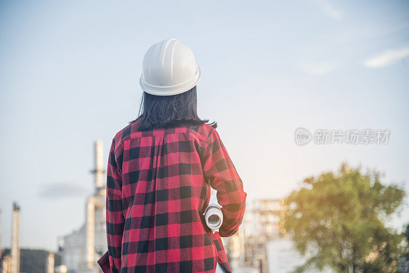 女工程师手持安全帽白色工作安全帽为建筑工程安全帽。炼油厂女工程师石油工业手握工人头盔安全帽。炼油工业工程