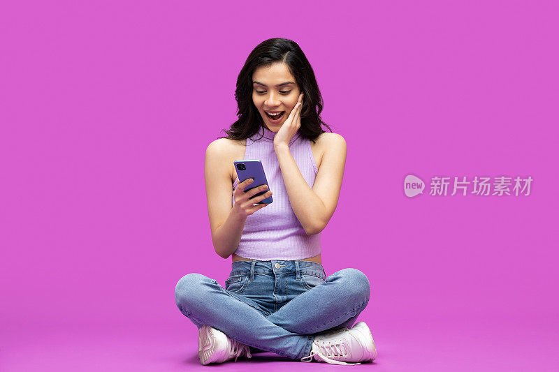 愉快的漂亮女孩使用手机的照片兴奋的紫色背景的股票照片
