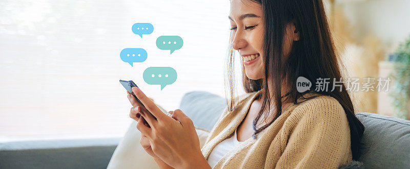 年轻的亚洲女性正在使用智能手机。聊天对话在聊天框图标弹出泡泡语音。社交媒体直接信息