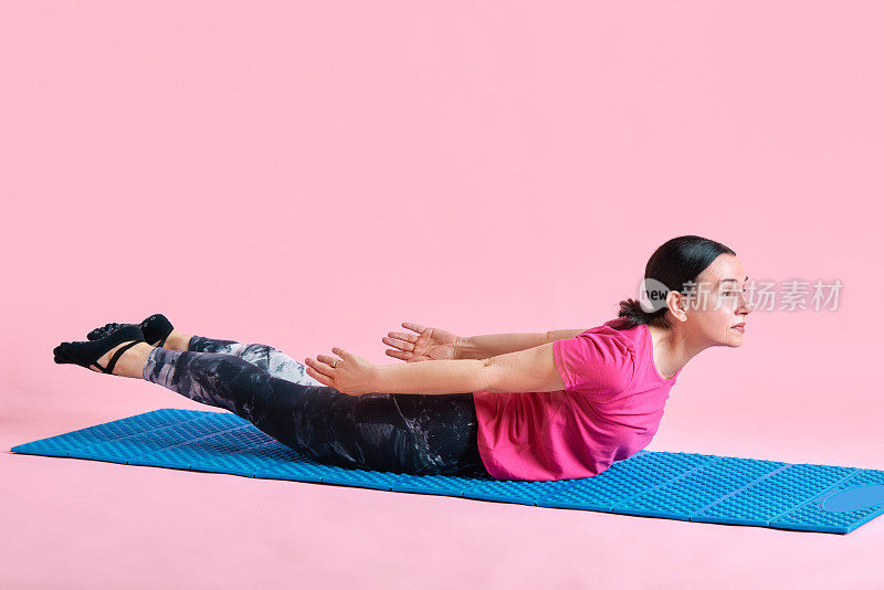 强壮的背部锻炼。成熟的女人躺在健身matt上，在粉红色的工作室背景下训练