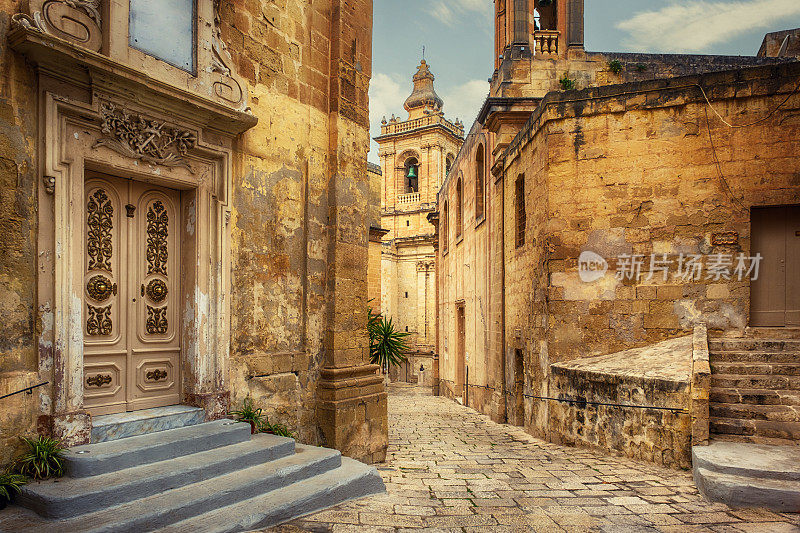 一条穿过地中海建筑的小巷，尽头是比古的圣劳伦斯教堂