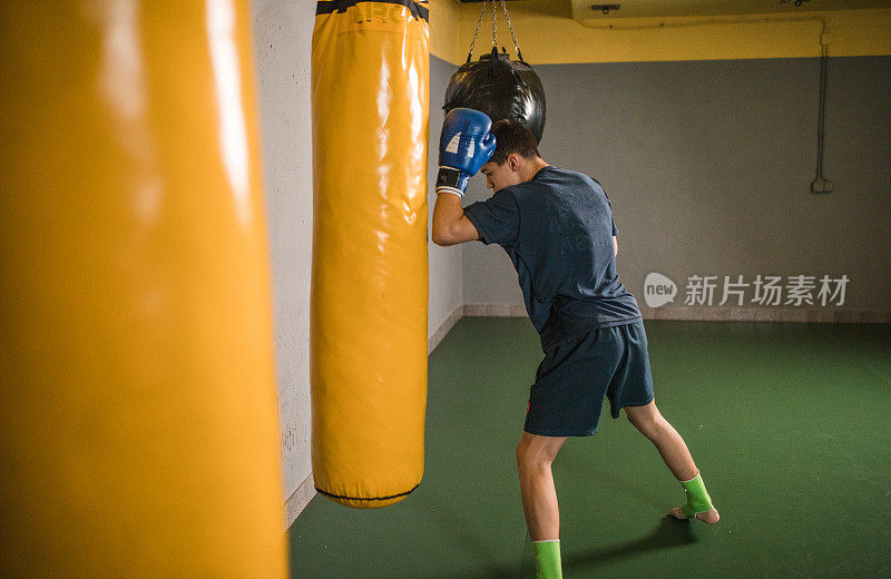 一个年轻的男子自由搏击运动员在健身房击打一个沙袋，以加强他的肌肉