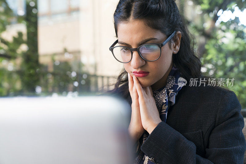 一个年轻女子被电脑显示屏包围着。一位女商人看着显示器上显示数据的移动图表，眼镜上的图像反射出来。