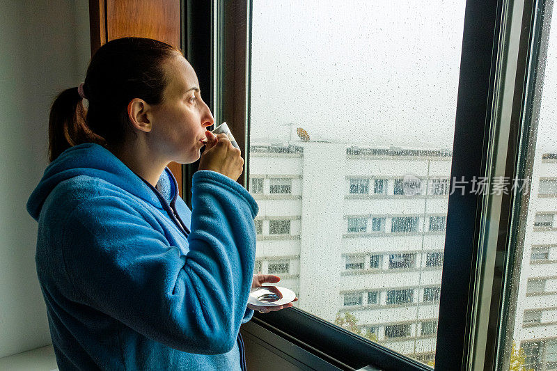 下雨天，一个手里拿着咖啡的女人望着窗外