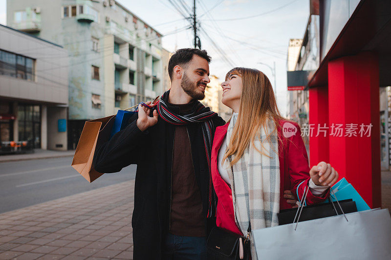 幸福的年轻夫妇拎着购物袋在城市里漫步
