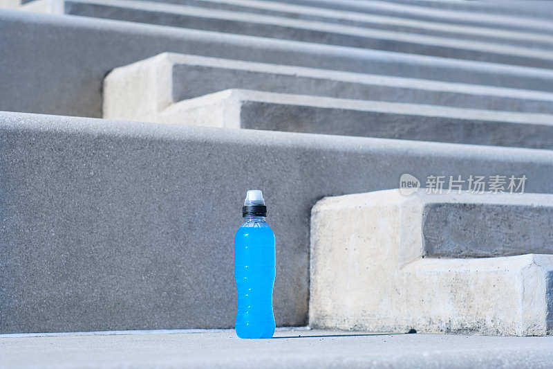 在一个阳光明媚的日子里，一个标准的透明塑料瓶PET，里面装着蓝色的能量饮料