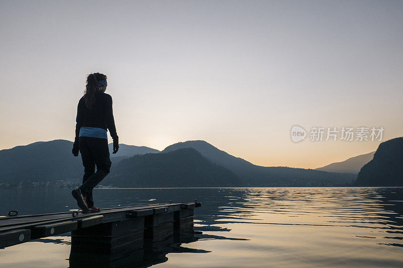 一个女人走到湖边的码头边，在山上和森林里看日出