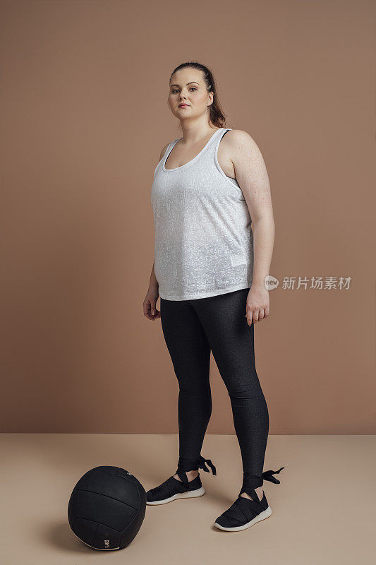 动机和决心:大尺寸的女人摆着一个药球，健身房的减肥概念
