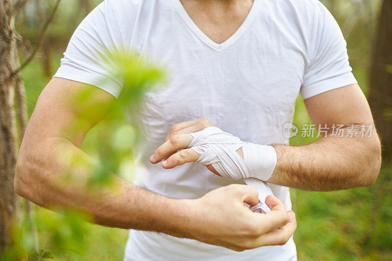 一个中年男子在森林里练拳击，绑上白色的拳击绷带，训练他的拳击技巧