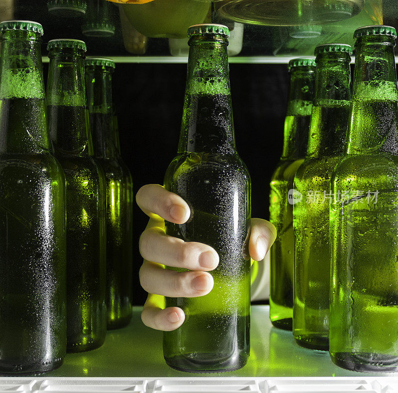 那只手伸向啤酒瓶。冰箱的架子上有绿色的啤酒瓶和凝结的水珠。