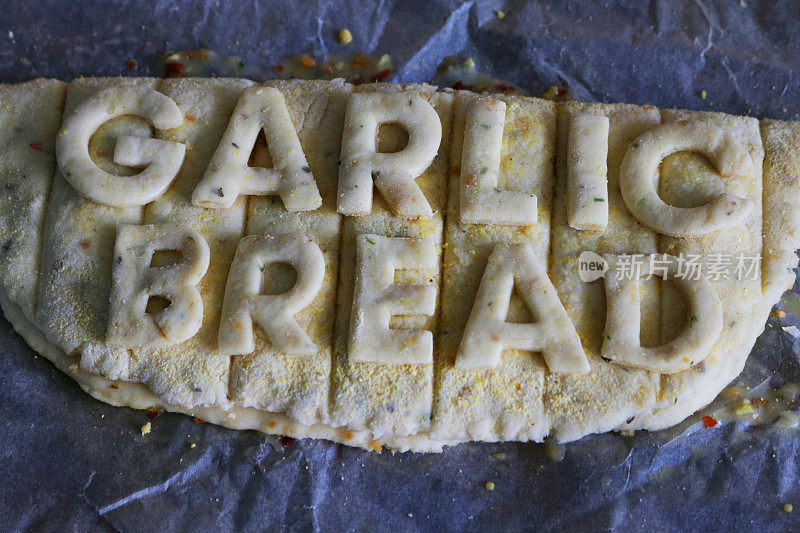 生蒜蓉面包的特写图片，贴着面团上剪下的字母，上面写着“蒜蓉面包”