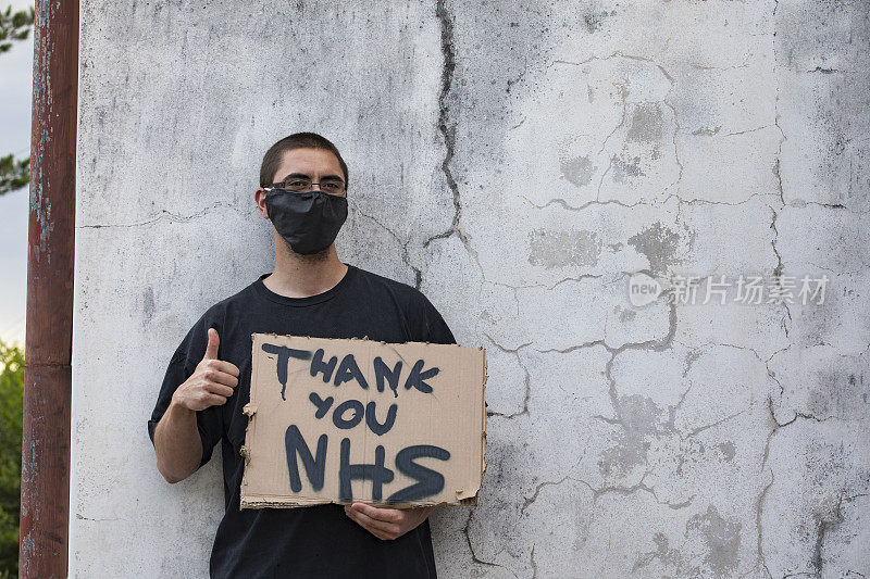 年轻的成年人显示拇指和拿着“谢谢你NHS”纸盒标志