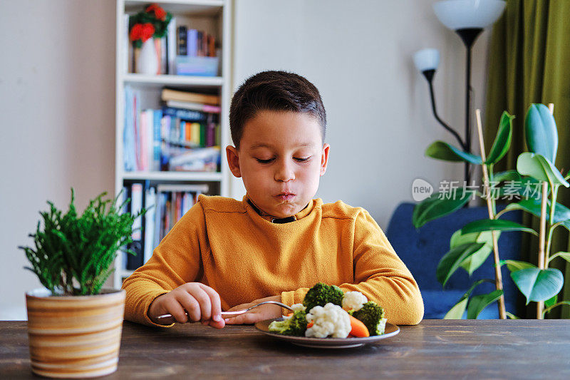 孩子对不得不吃蔬菜很不高兴。他的盘子里有许多蔬菜。他讨厌蔬菜。