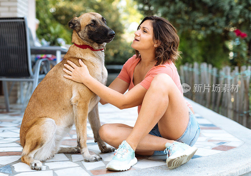 成熟的女人和她的狗说话-白种女人和比利时牧羊犬在后院