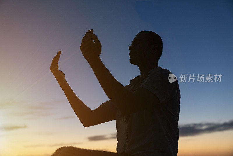 日落时分，穆斯林男子在山顶祈祷的剪影