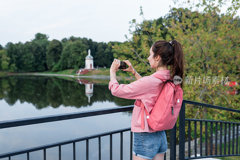 一名女子在城市的湖边、河边和池塘边避暑，用智能手机拍摄风景，在互联网上录制视频，这是一款智能手机的应用。为文本副本提供空闲空间。