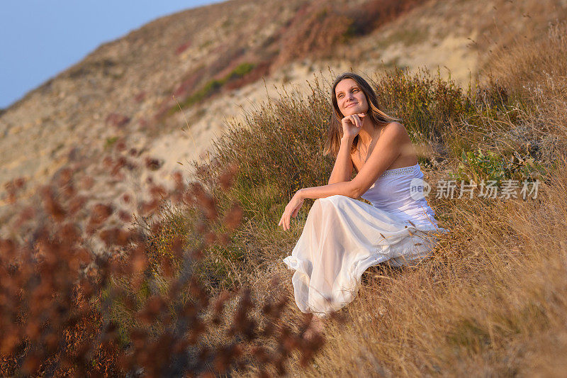 一个穿着白色连衣裙的女孩欣赏着美丽的日落景色