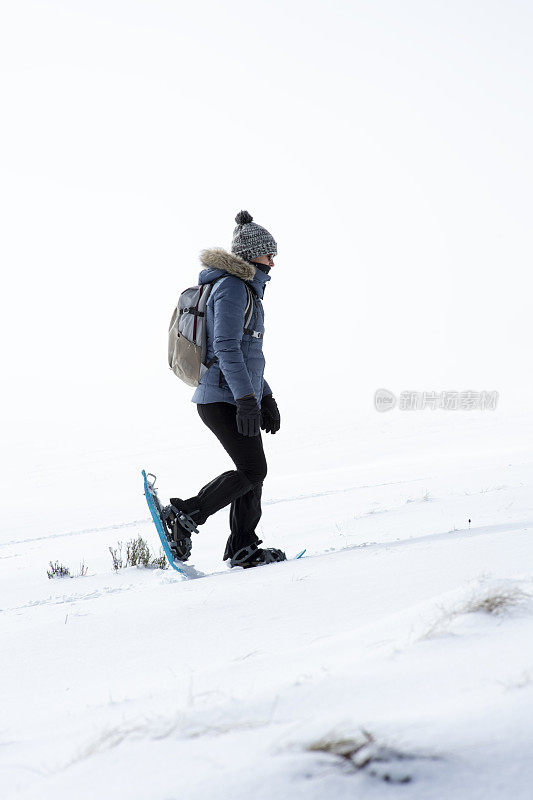 一个穿着雪鞋的女人爬上了白雪覆盖的斜坡