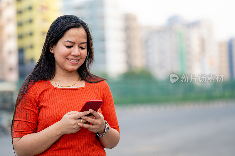 在背景为建筑物的城市里，用智能手机发短信或读短信的女人面带微笑。