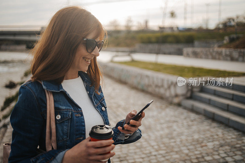 年轻女子在城市码头上用智能手机喝着外卖咖啡