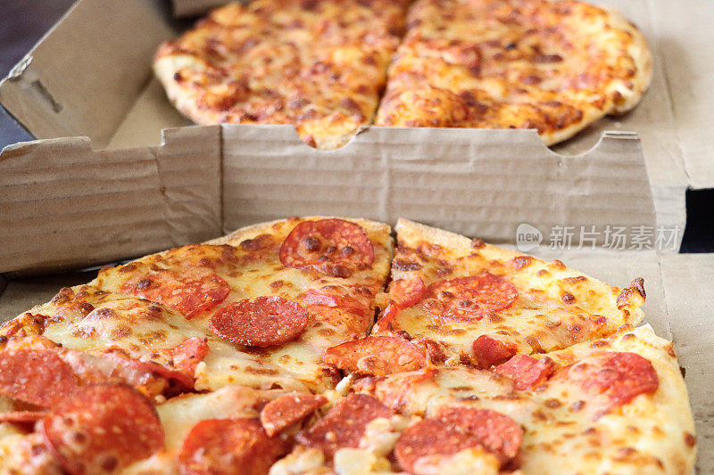全帧图像的两个切片披萨在纸板外卖披萨盒，意大利辣香肠和玛格丽塔披萨，重点在前景
