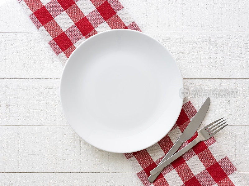 直接俯瞰空的白色陶瓷餐盘在红白格子花格桌布上质朴的白色木桌背景刀和叉旁边的盘子。