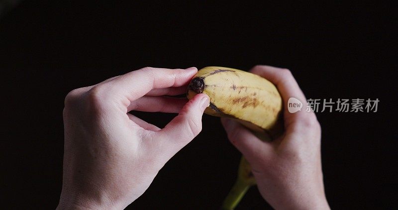 人类的双手正在剥香蕉。在黑色背景下的个人观点