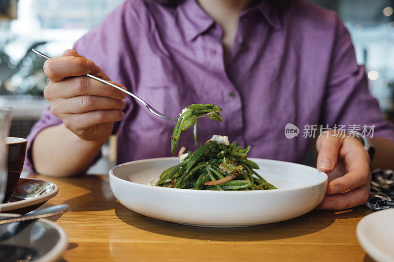 一名匿名女子拿着叉子在餐厅吃午饭的裁剪照片