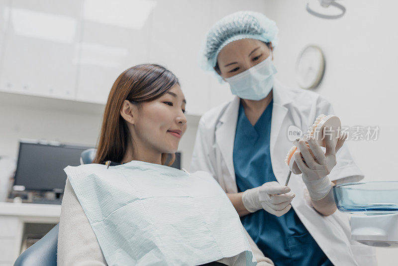 医疗保健-亚洲女性病人审查她的牙齿咨询她的牙医，专注于牙齿模型