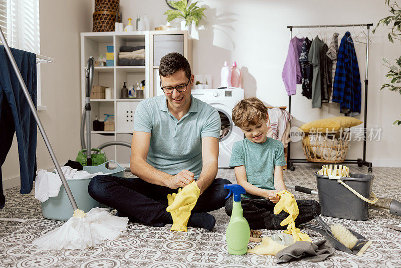一个小男孩微笑着帮爸爸擦地板。孩子把橡胶黄色手套戴在手上，他们一起用布和液体清洗污垢灰尘