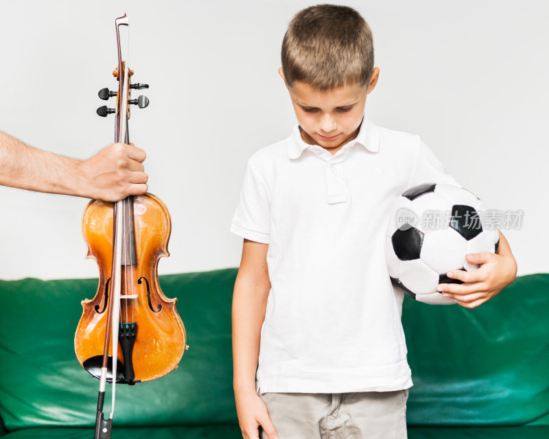 一个小男孩拿着一个足球，递给他一把小提琴