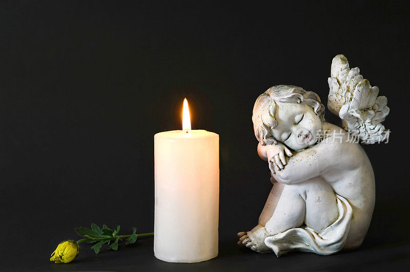 白色的蜡烛，一个天使和花在黑暗的背景