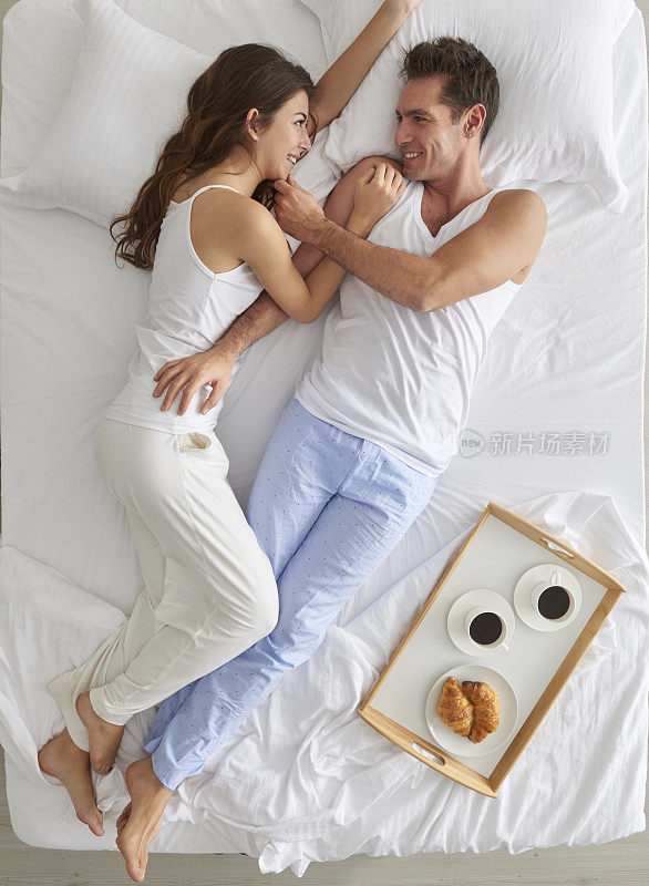 一对夫妇躺在床上，端着早餐盘
