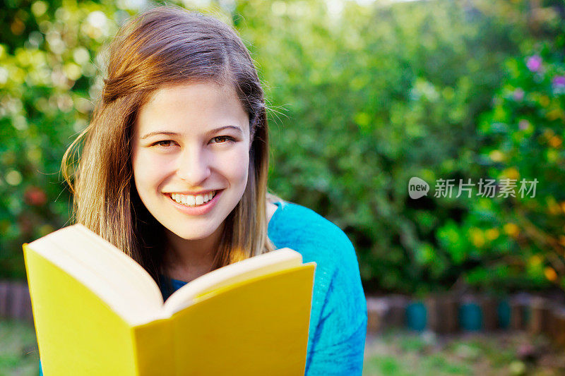 微笑的年轻读者的肖像在花园与打开的书