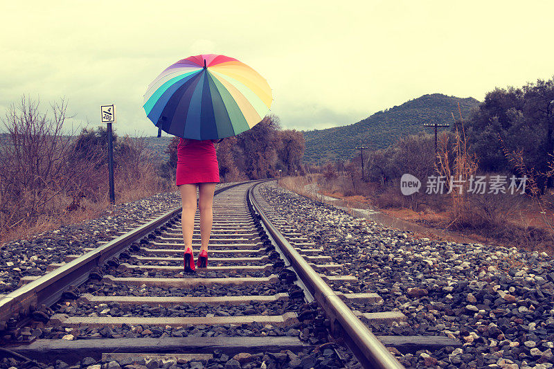 穿红色衣服的女人拿着五颜六色的雨伞在铁路上走