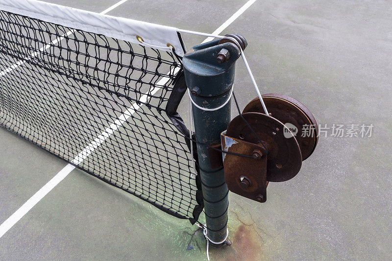 网球网生锈的绞车柱在褪色的球场上的特写