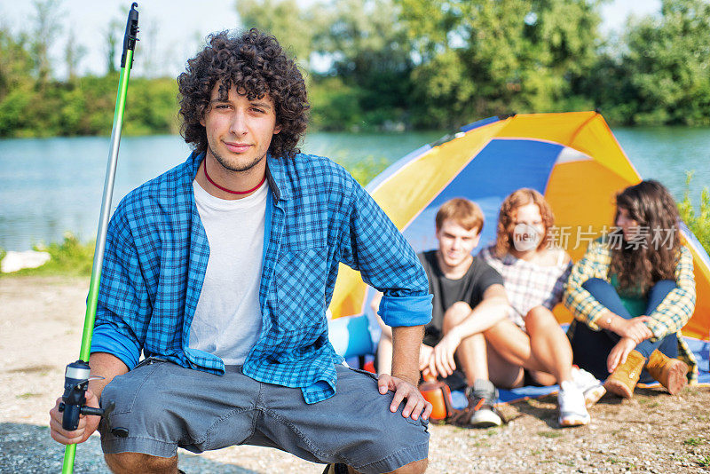露营:年轻人拿着钓竿。帐篷里的朋友