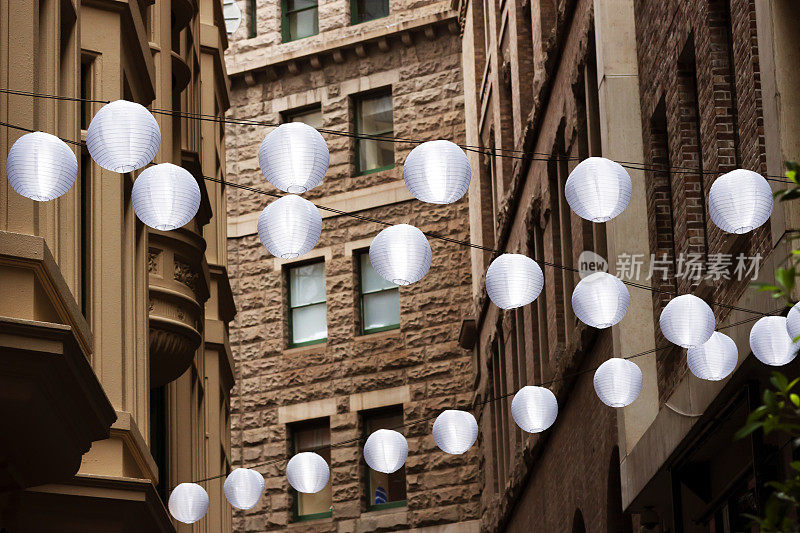 一排排的白色灯笼悬挂在建筑物之间的街道上