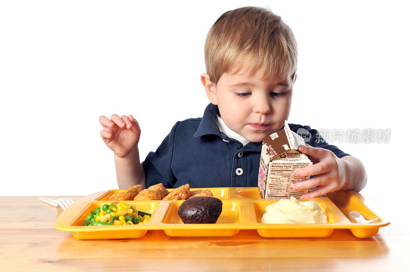 小男孩坐在桌子旁和他的学校午餐