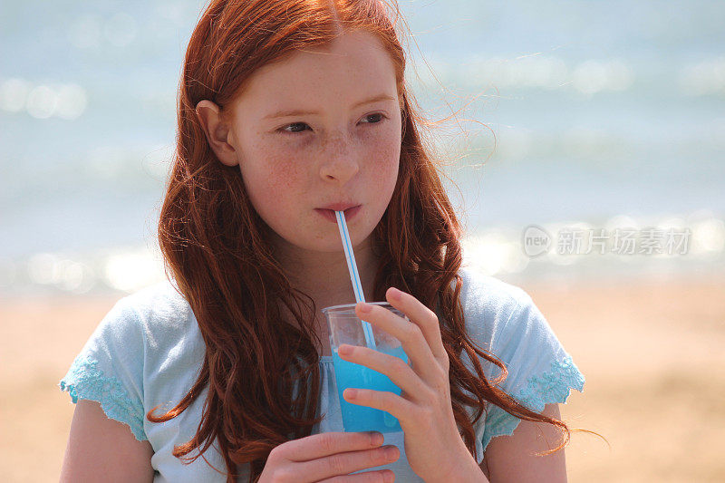 女孩在海滩上用吸管喝冰沙饮料，冰冻的冰饮料