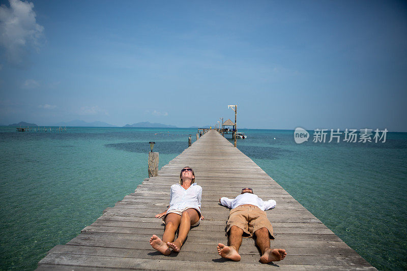 一对年轻夫妇在热带风景的木制码头上休息