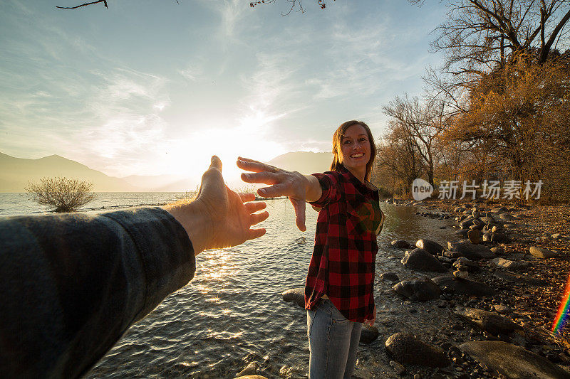 年轻女子走在湖边，牵着一个男人的手