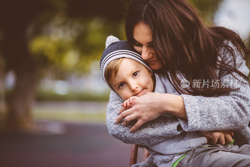 年轻的黑发母亲在公园里拥抱着她的小儿子